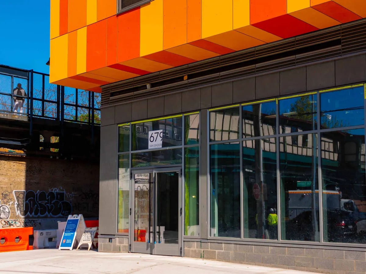 Ground-floor retail storefront with full-height glazed aluminum framing and a glass entrance door beneath a coloured canopy.